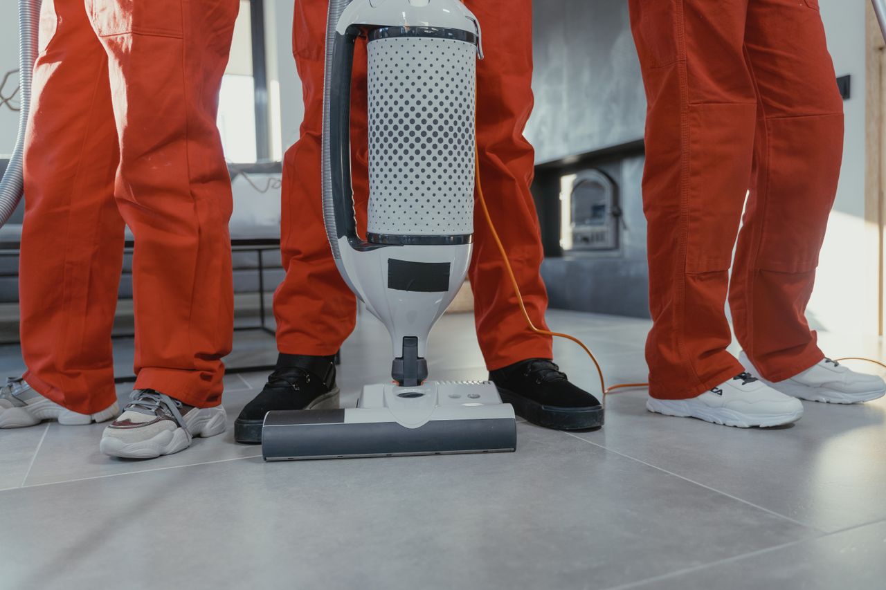 Professional cleaning team in red uniforms using a vacuum cleaner indoors.